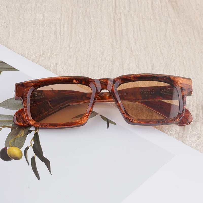 Tortoiseshell sunglasses on a light surface with green leaves